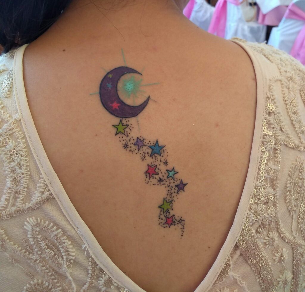 Tatuagem de lua roxa, estrela azul e pequenas estrelas nas costas