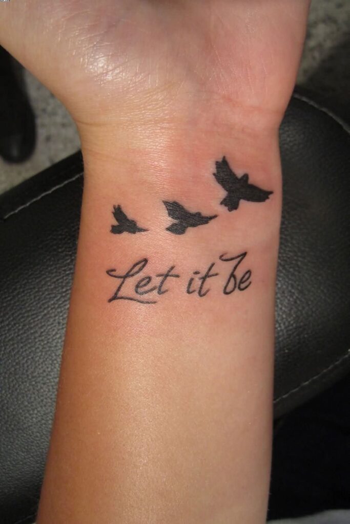 Tatuaggio sul polso di una donna con uccelli e la scritta Let it be Let it be in inglese