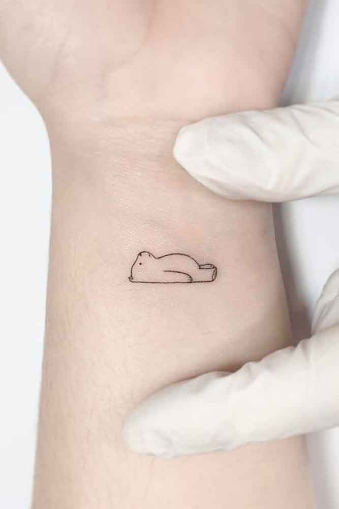 Tatuagem no pulso feminino, contorno de um urso deitado