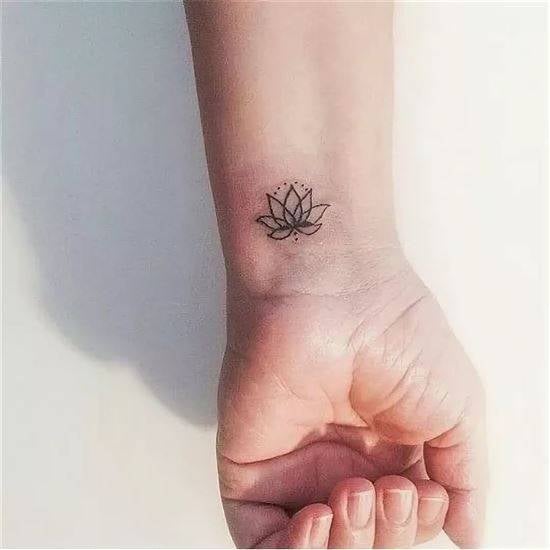 Tatuagem de pequena flor de lótus no pulso feminino