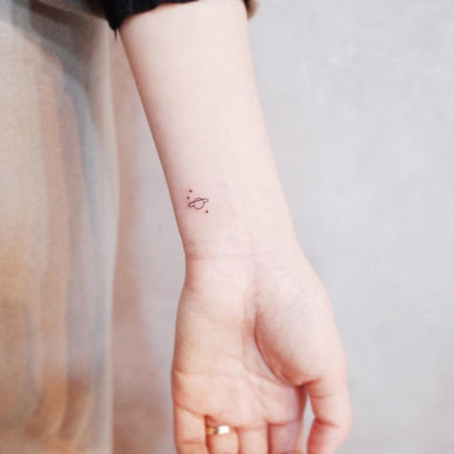 Tatuagem no pulso de mulher minúsculo planeta tipo Saturno e estrelas