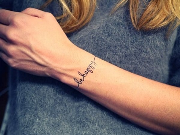 Tatuaggio sul polso di una donna con un braccialetto con la scritta Be Happy in inglese