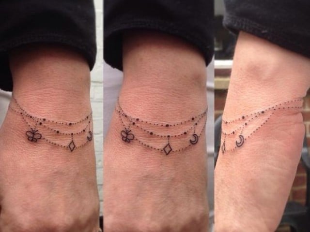 Tatuaggio a forma di braccialetto sul polso di una donna con tre catene di farfalle e rombi pendenti
