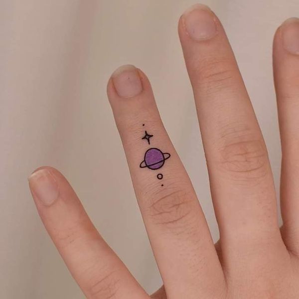 Tatuagem de Saturno nos dedos em violeta e estrelas