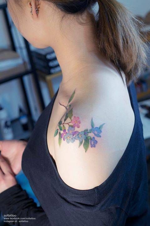 Tattoo on Shoulder Woman Delicate Little Blue Flowers Roses Branches and Green Leaves