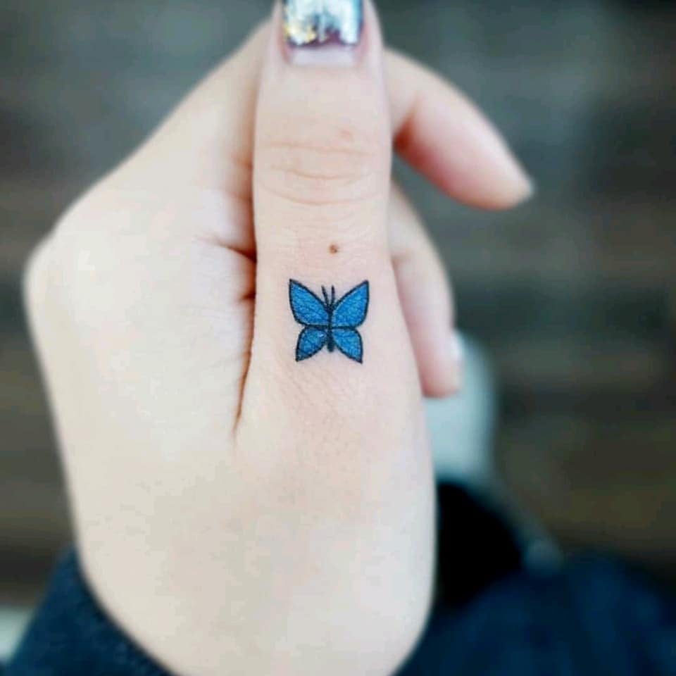 Ästhetische Tattoos. Wunderschöner kleiner minimalistischer blauer Schmetterling am Daumen