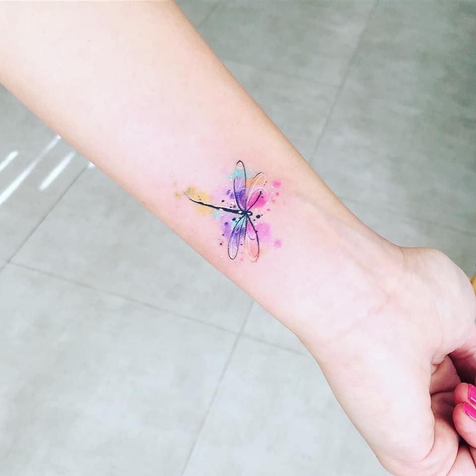 Pequenas tatuagens finas mulher libélula colorida no pulso