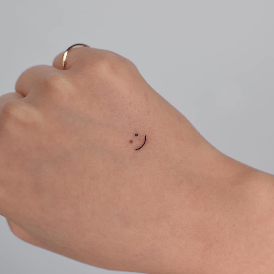 Tatuagens Minimalistas Super Pequenas Carinha sorridente na mão apenas contorno da boca e dois pontos dos olhos