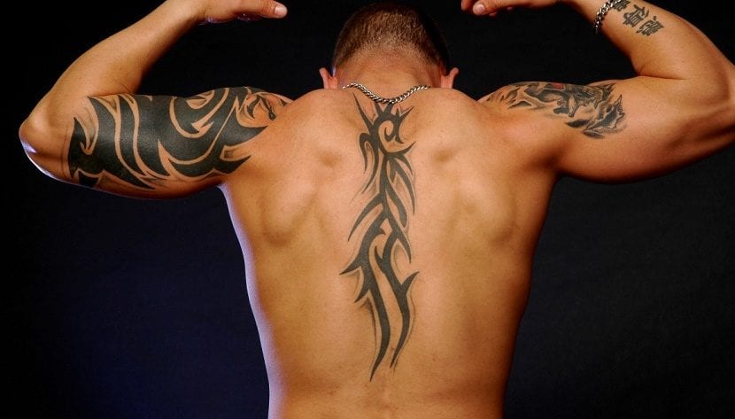 Tribal tattoos on the back along the spine and on the arms of a man