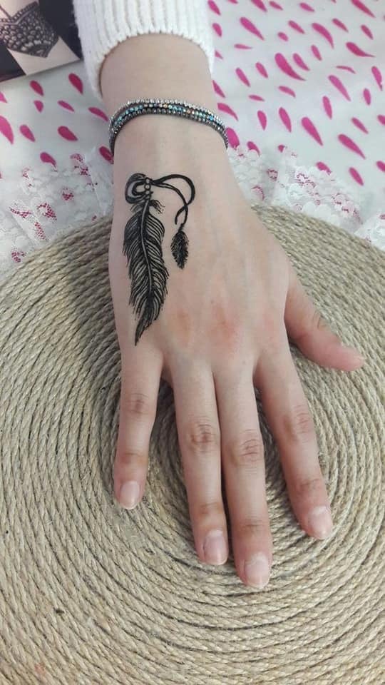 Tatuajes bellos para mujeres pluma negra en mano
