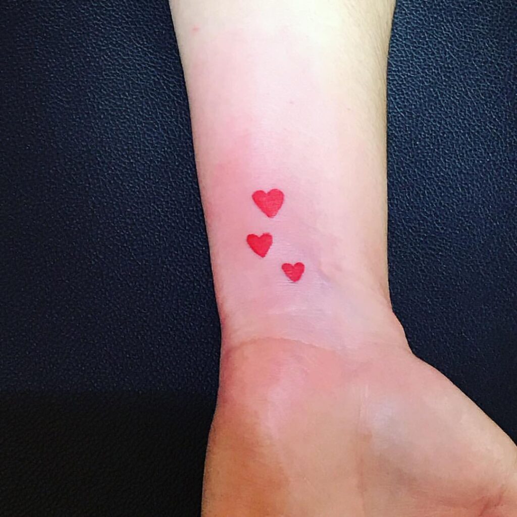 Piccoli tatuaggi a tre cuori rossi intensi sul polso