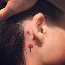 Piccolissimi tatuaggi rossi di tarassaco dietro l'orecchio