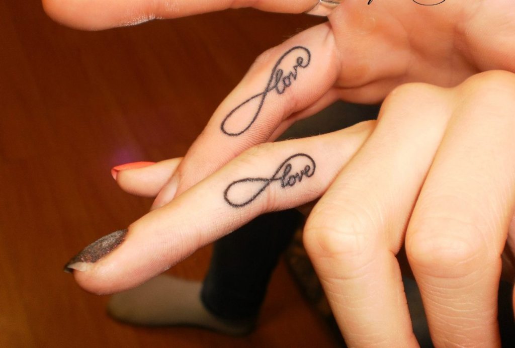 Unendlichkeits-Tattoos auf zwei Fingern beider Hände mit dem Wort „Love Love“.