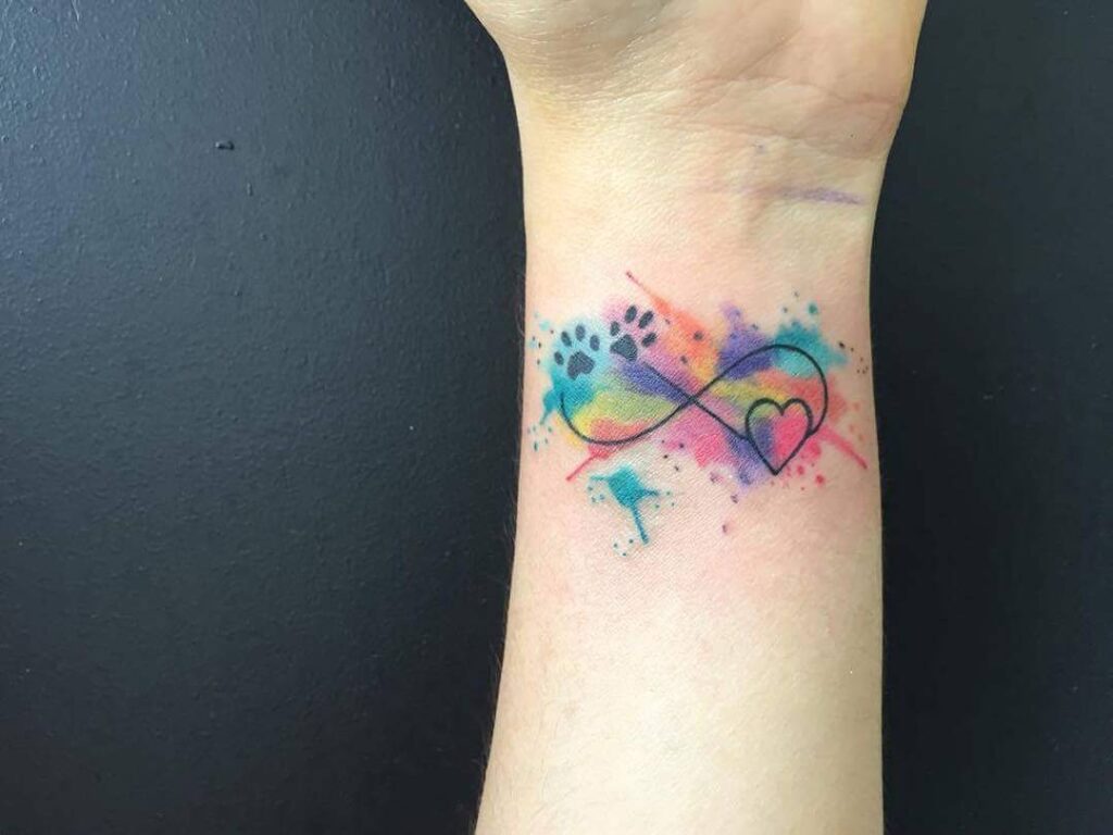 Tatuaggi infinito in stile acquerello con cuore e zampe di cane sul polso