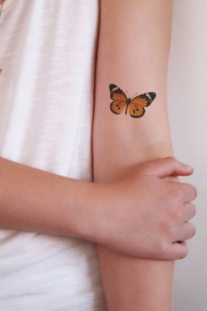 Orangefarbene Schmetterlings-Tattoos auf dem weiblichen Arm 1