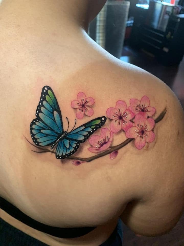 肩のピンクの花の小枝に止まっている蝶のタトゥー