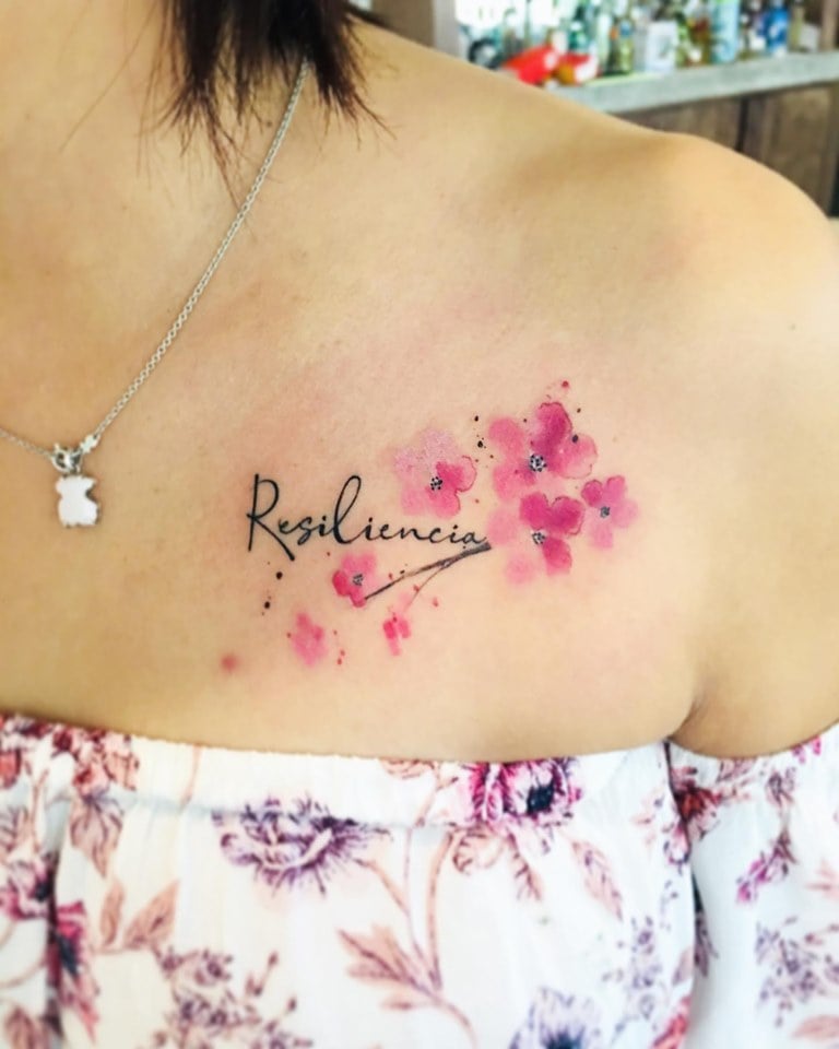 Tatuajes de Resiliencia Destacada 2 en la clavicula la palabra con flores rosas