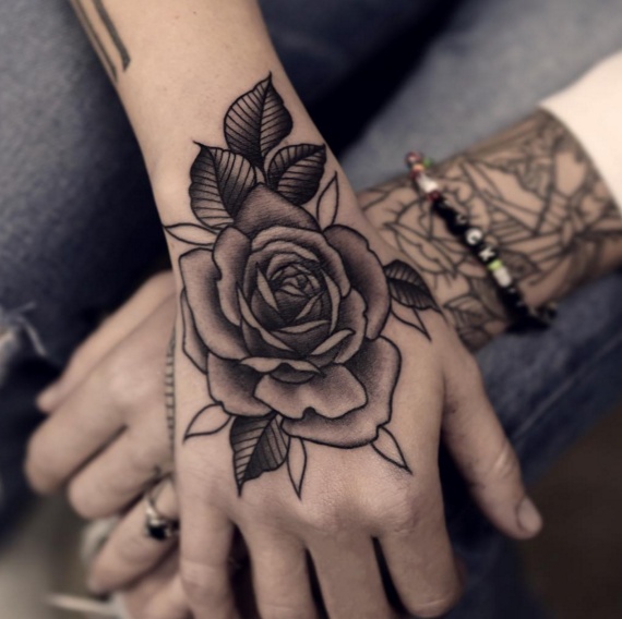 Tatuagens de rosas negras nas mãos grandes em todo o dorso da mão