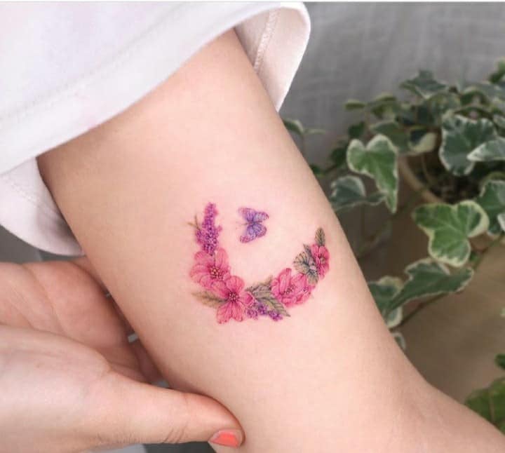 Tattoos of delicate crescent flowers of pink flowers and violet butterfly on arm
