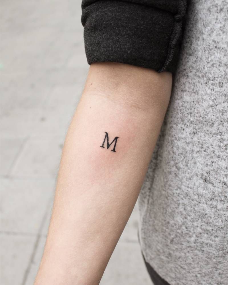 Tattoos of the letter M eme in uppercase printing on forearm