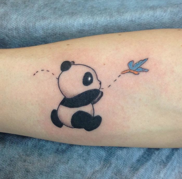 Tatuagem de urso panda no antebraço perseguindo uma borboleta