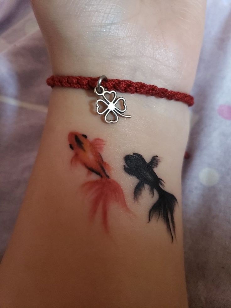 Schwarze und rote Fisch-Tattoos am Handgelenk