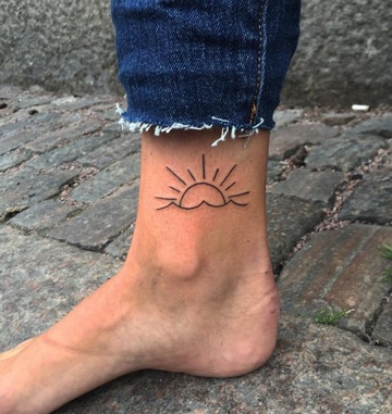 Tatuagens no horizonte do mar da mulher do tornozelo e contorno do sol
