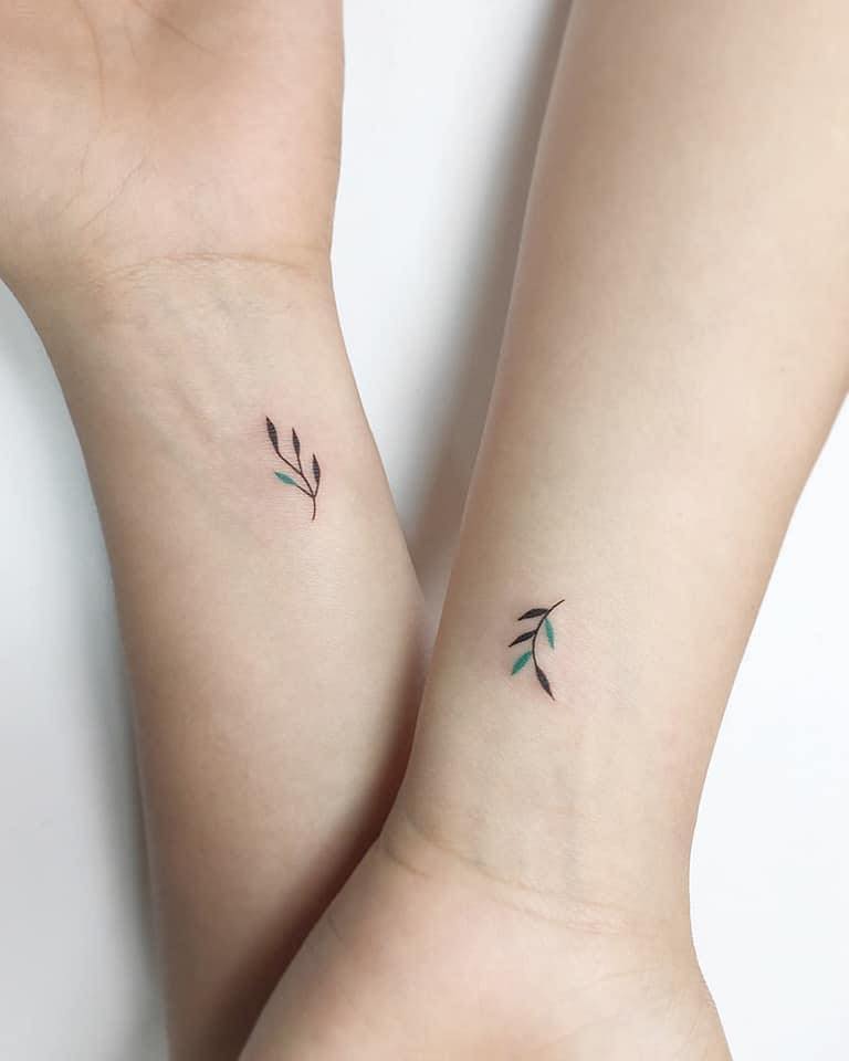 Tatuaggi minimalisti per coppie sorelle cugine amiche due ramoscelli con dettagli verdi sui polsi
