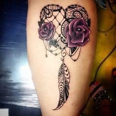 Dreamcatcher tattoos for women in the shape of a heart with two purple flowers and a feather
