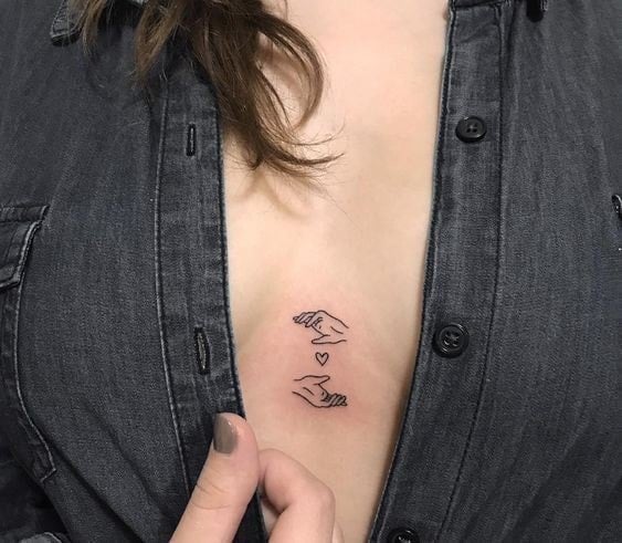 Pequenas tatuagens femininas mãos e coração no meio do peito