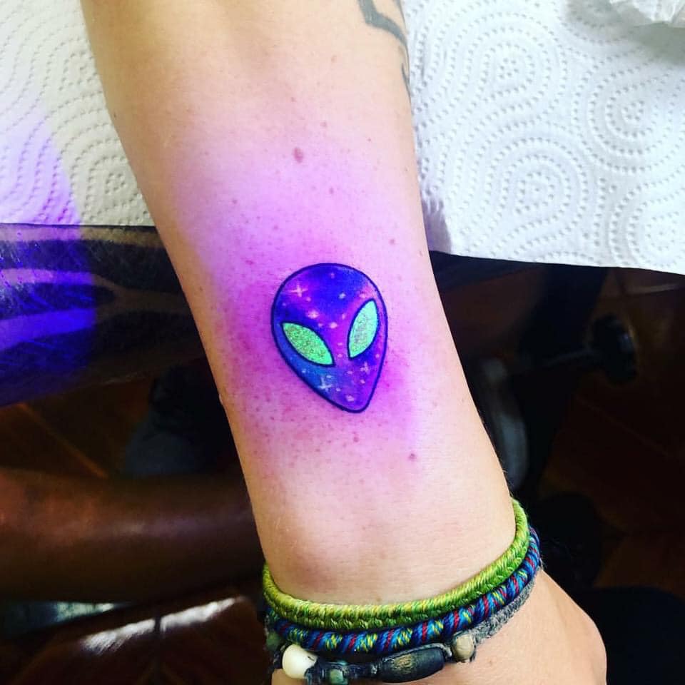 Tatuagens de rosto alienígena brilhante na panturrilha