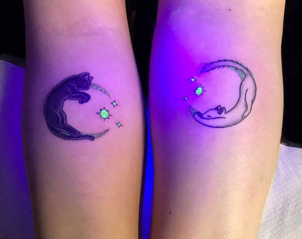 Leuchtende Tattoos: Schwarze Katze und weiße Katze mit Details leuchtender Sterne