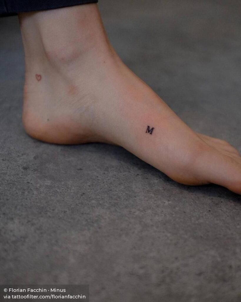 Delicate tattoo on foot area of a tiny woman letter m