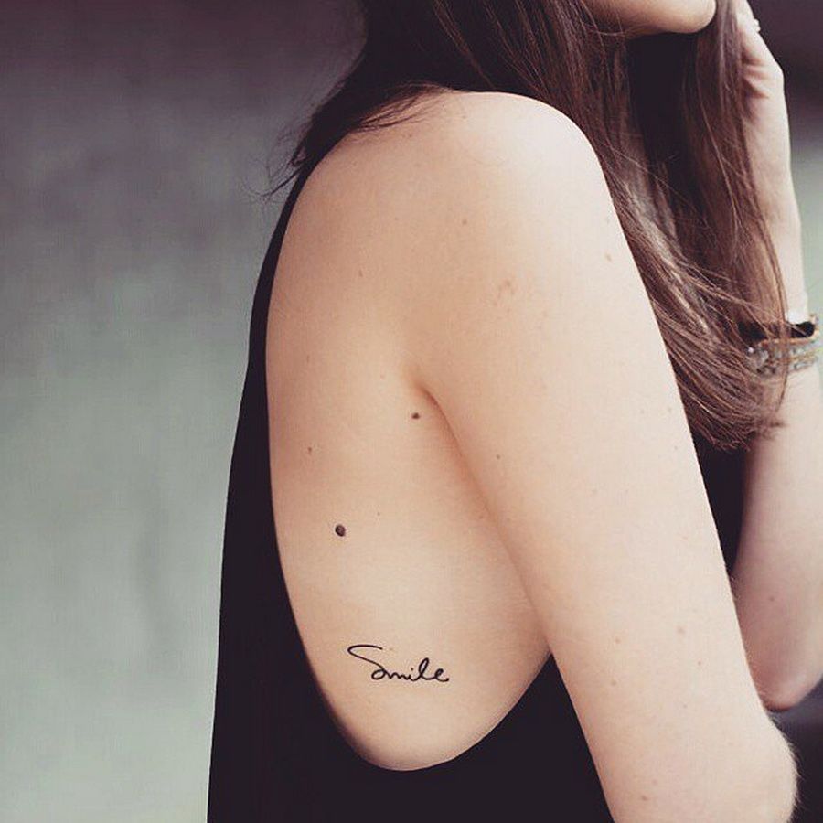 tatuaje en la costilla pequena inscripcion de Smile en mujer